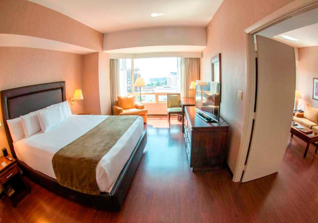 Habitación de hotel con cama grande y sala de estar. en Hotel Clarion Suites Guatemala, en Guatemala