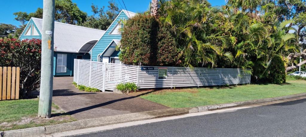 a white fence in front of a house with palm trees at Twin Peaks 1 in Blueys Beach