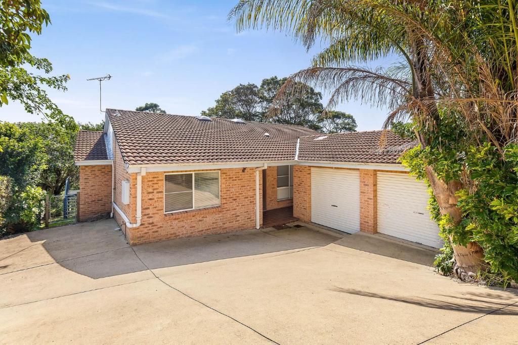 ein Backsteinhaus mit zwei Garagentoren und einer Palme in der Unterkunft 1-3A Montague Street, Narooma in Narooma