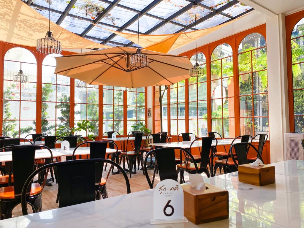 uma sala de jantar com mesas, cadeiras e janelas em SO Zen Hotel Silom Bangkok em Bang Rak