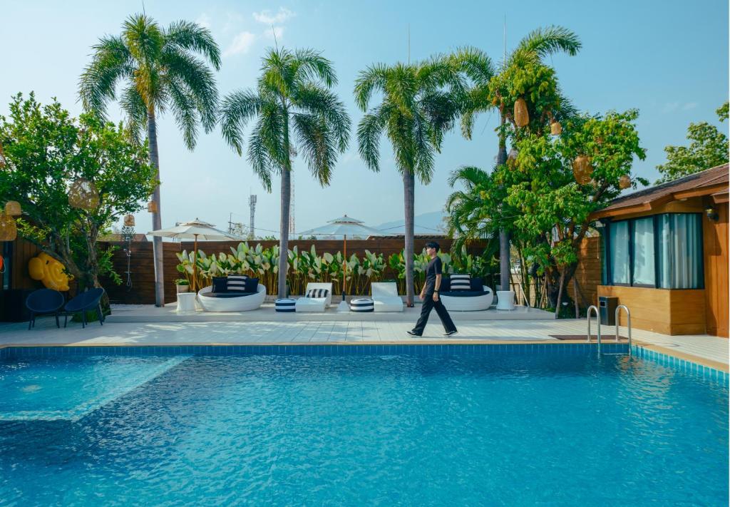 a man walking by a swimming pool with palm trees at R1 Resort Rajapruek Chiangmai in Chiang Mai