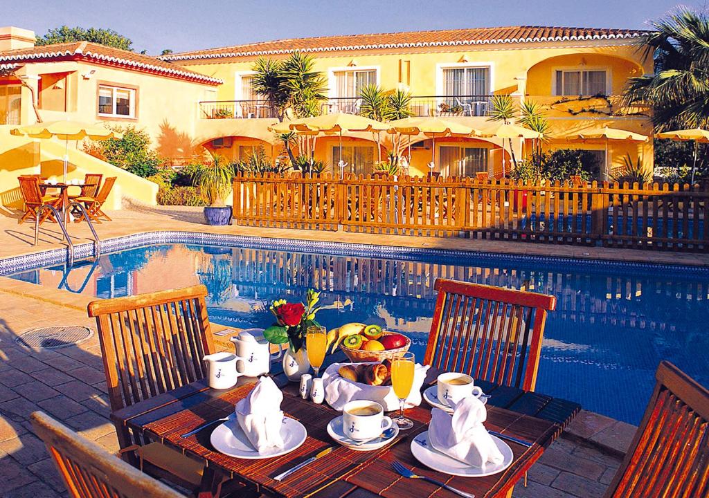 a table with a breakfast of coffee on it next to a pool at Costa d'Oiro Ambiance Village in Lagos