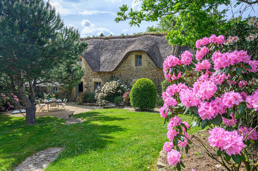 ein Steinhaus mit einem Strohdach mit rosa Blumen in der Unterkunft Charmante longere pour un doux sejour in Pluvigner