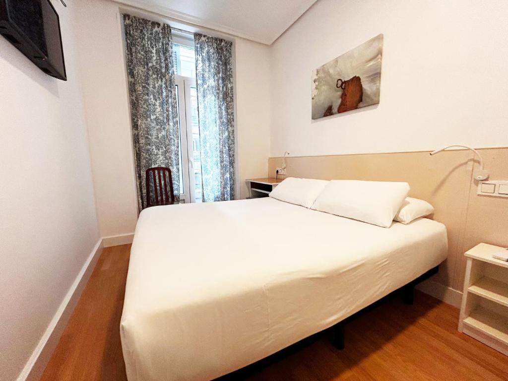 a bedroom with a white bed and a window at Pensión Régil in San Sebastián