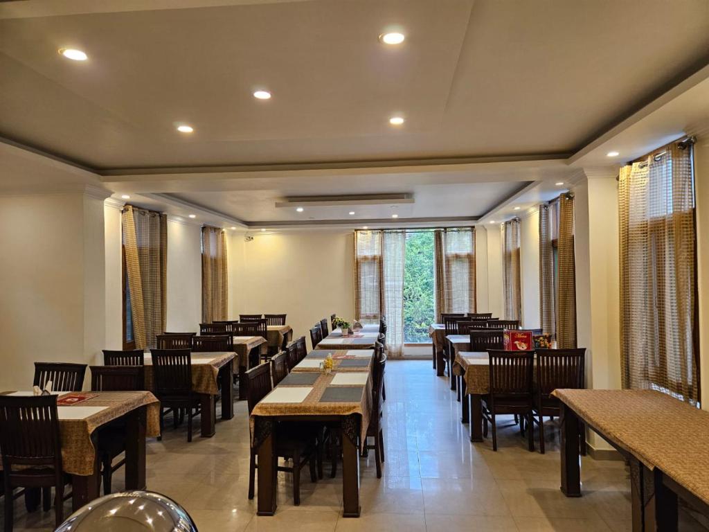 a dining room with tables and chairs and windows at Hotel Akash Regency in Manāli