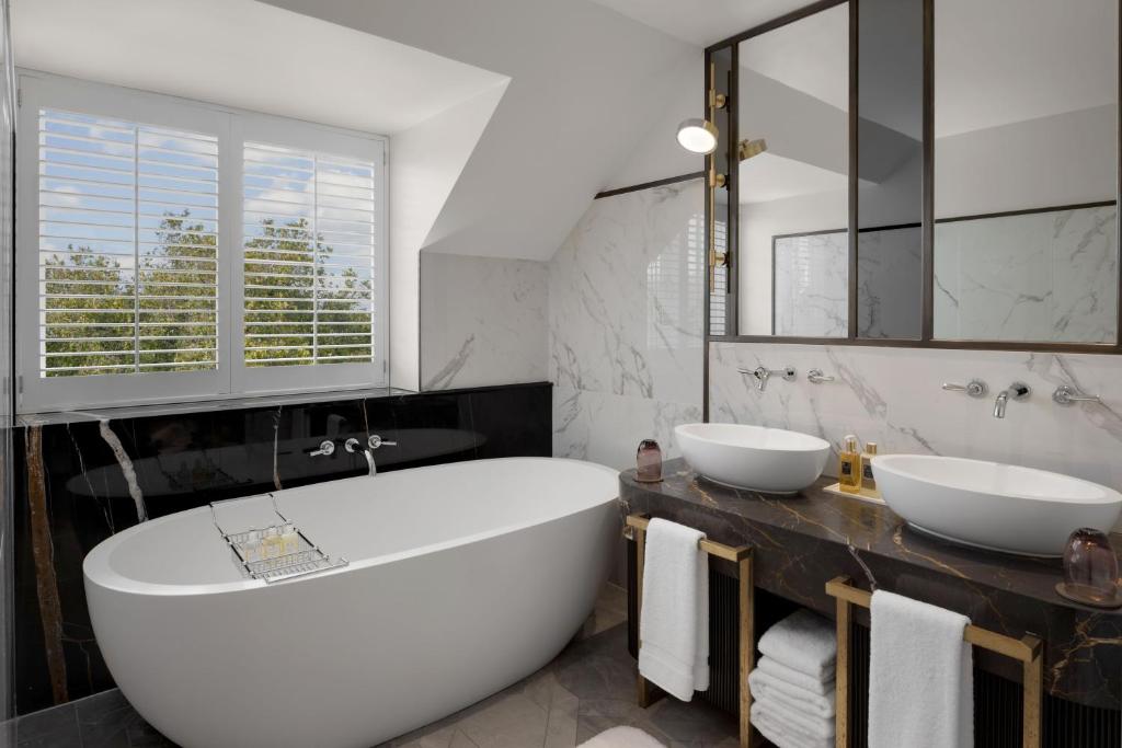 a bathroom with a large white tub and two sinks at The Biltmore Mayfair in London