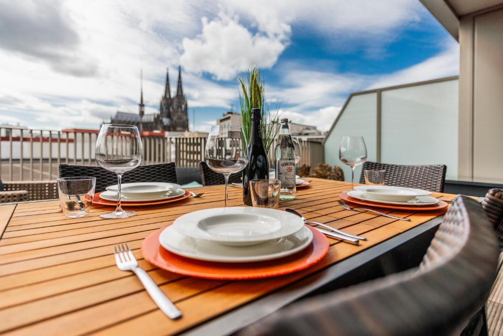 ケルンにあるExklusives Luxus Loft am Dom - Dachterrasse mit Traum-Aussichtの木製テーブル(皿付)、バルコニー(ワイングラス付)