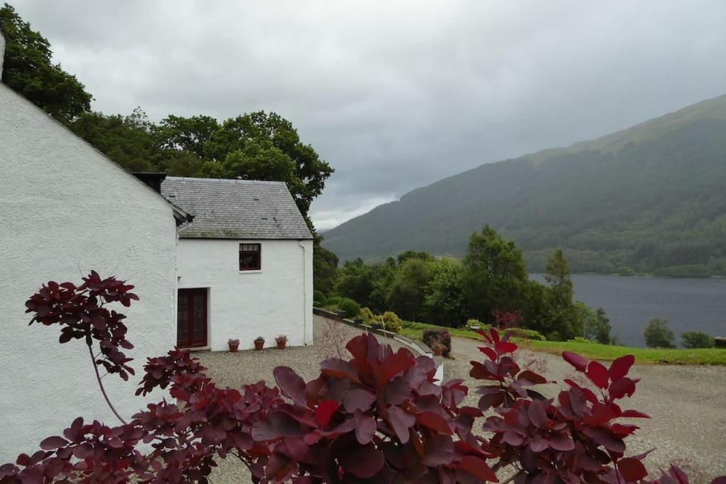 a small white house with a view of a lake at Craigruie Farmhouse in Balquhidder