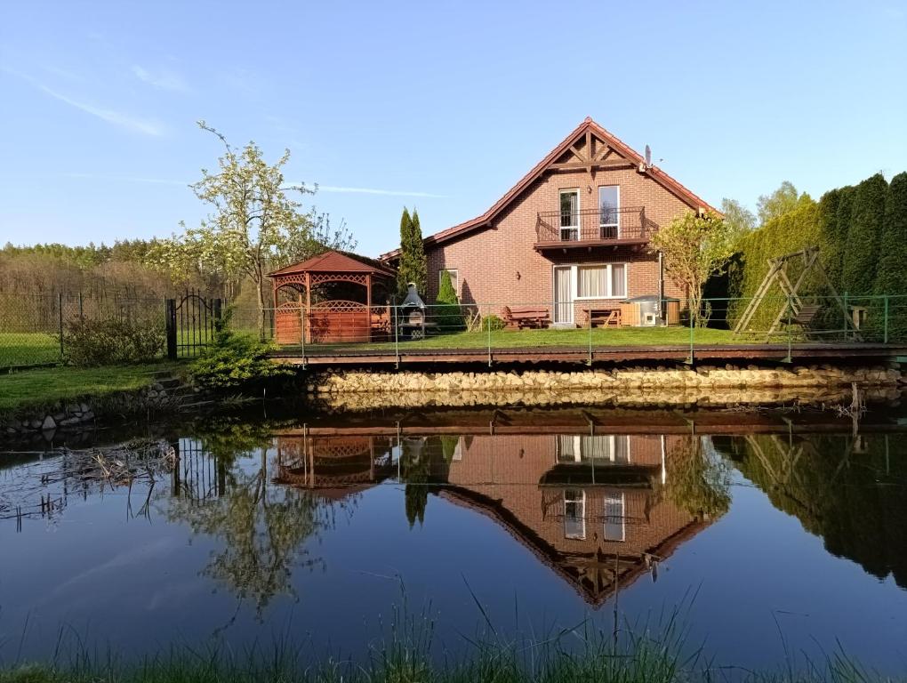 uma casa com um reflexo na água em Domek nad stawem z balią i sauną em Suleczyno