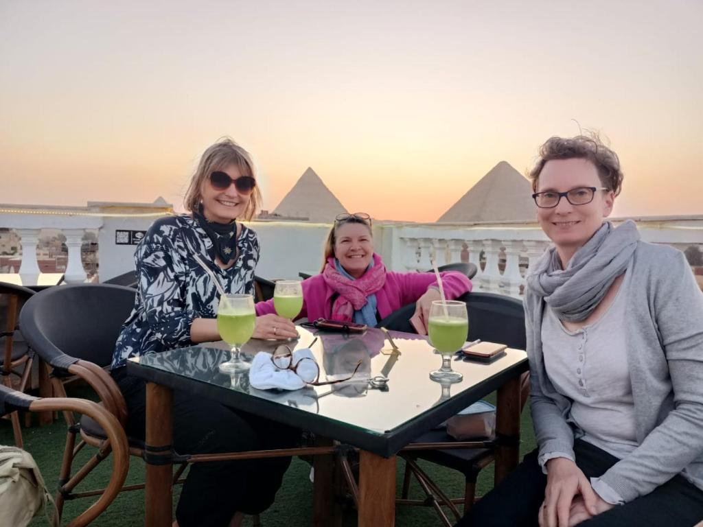 tres personas sentadas en una mesa frente a las pirámides en Pyramid stars inn en El Cairo