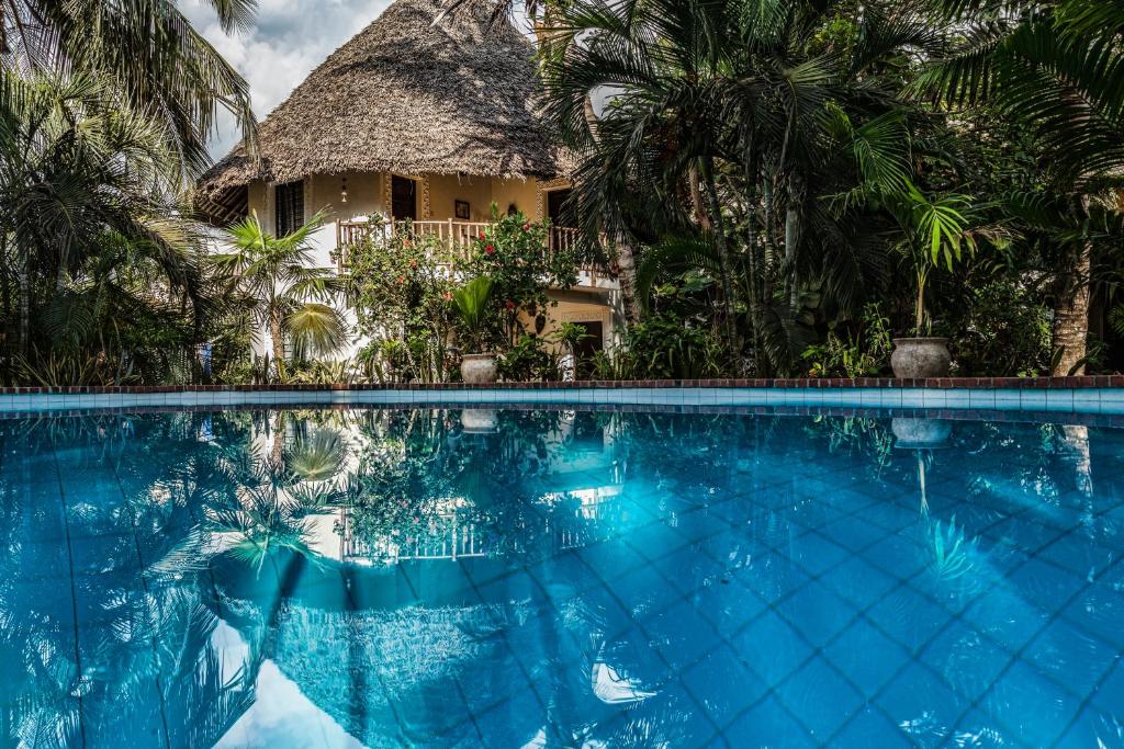 a resort swimming pool with a thatch roof at Diani Villa in Diani Beach