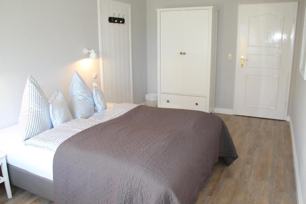 a white bedroom with a large bed with blue pillows at Landhaus Nordstern Hotel garni in Utersum