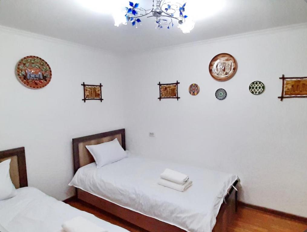 Duas camas num quarto com paredes brancas e um lustre em Guesthouse Anora em Samarkand