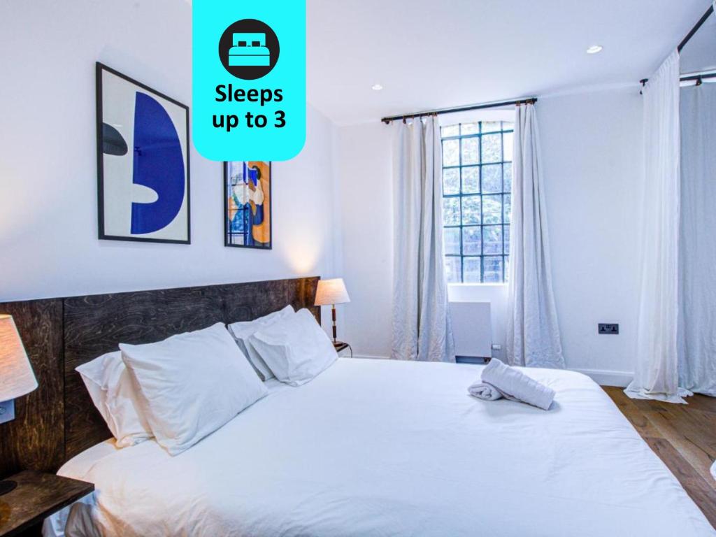 a bedroom with a bed with white sheets and a window at Charming 1BR Apartment in a gated complex and a short walk from Queens Park Tube in London