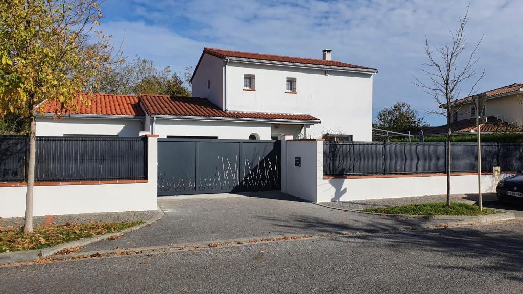 une maison blanche avec un portail et une clôture dans l'établissement Chambre avec cuisine indépendante à 25 min du capitole, à Auzeville-Tolosane