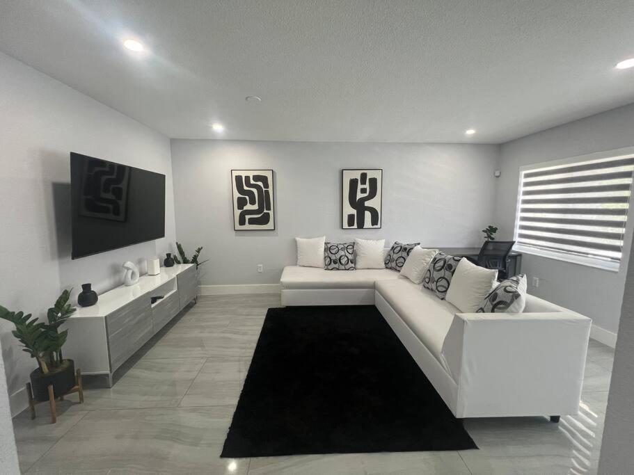 Stadium Chic Oasis: Modern Retreat in Miami close to Beaches في ميامي غاردنز: غرفة معيشة مع أريكة بيضاء وتلفزيون
