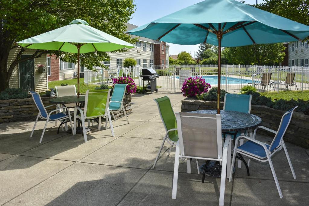 un patio con tavoli, sedie, ombrelloni e piscina di Cresthill Suites Syracuse a East Syracuse
