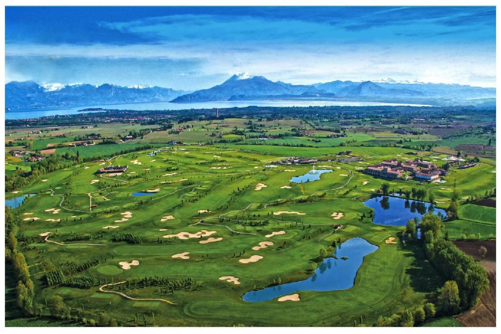 - une vue aérienne sur un parcours de golf avec un lac et des montagnes dans l'établissement Green and Relax, à Pozzolengo