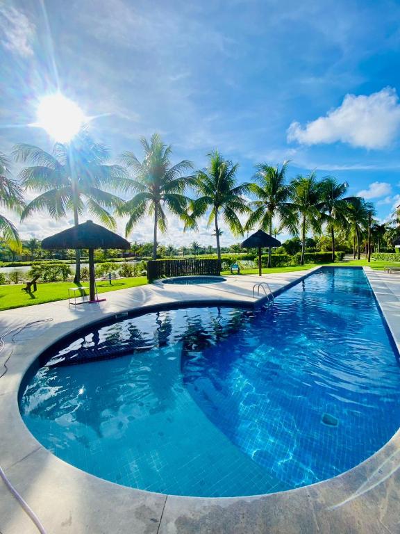 a large swimming pool with palm trees in the background at Refúgio na Praia do Forte in Praia do Forte
