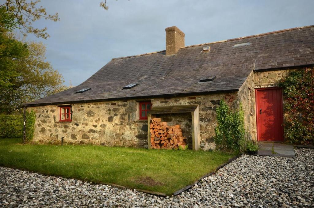 una casa de piedra con puertas rojas y un montón de troncos en The Longhouse, en Pwllheli