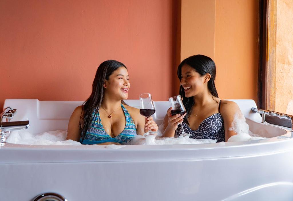 zwei Frauen sitzen in einer Badewanne mit Weingläsern in der Unterkunft Campo Lago Hospedaje in Otavalo