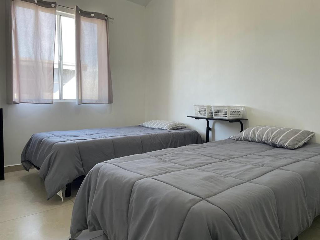 two beds in a white room with a window at Habitaciones en Casa Casiopea in Tijuana