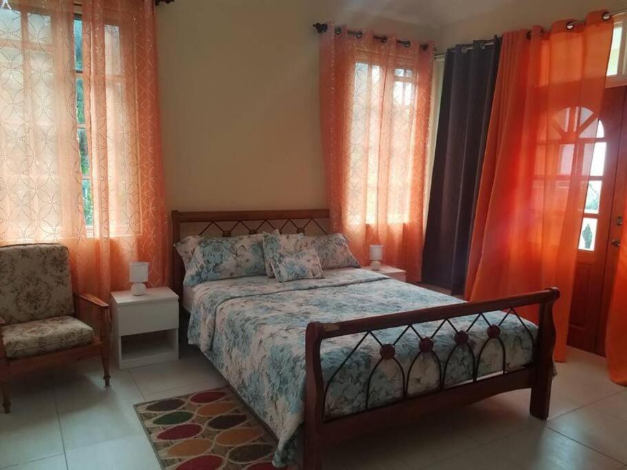 a bedroom with a bed and a chair and windows at The Essence of Quiet and Comfort in Roseau