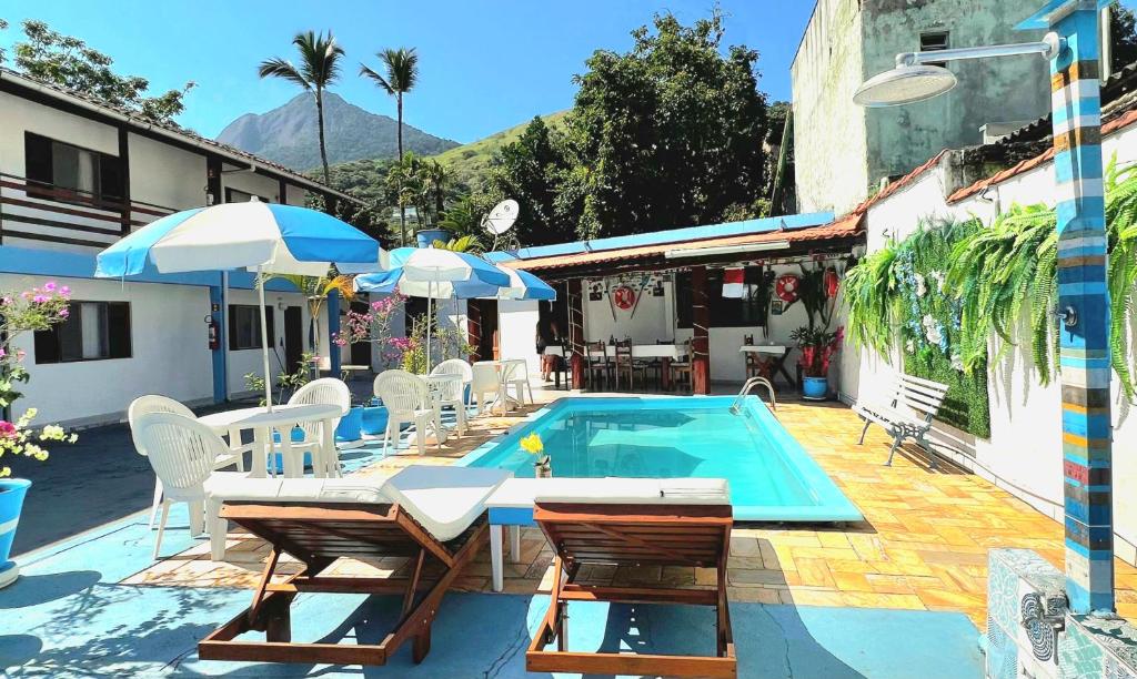 a swimming pool with chairs and a table and umbrella at Suítes Nova Mar Ilhabela in Ilhabela