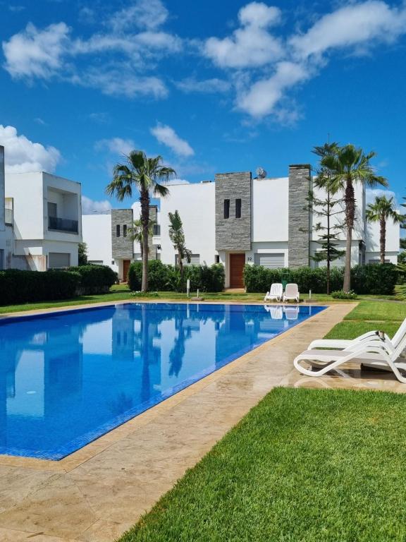 a swimming pool in front of a building with palm trees at Villa blancha beach sidi rahal in Sidi Rahal