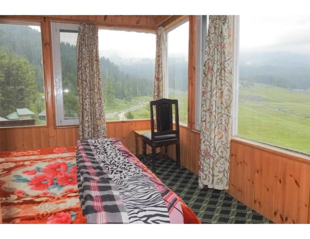 een slaapkamer met een bed en een stoel voor een raam bij Hotel Yemberzal & Restaurant, Jammu and Kashmir in Gulmarg