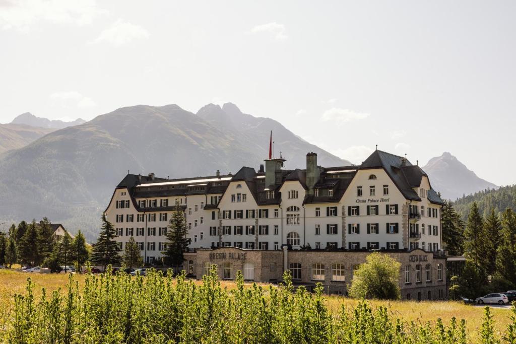 a large building in a field with mountains in the background at Cresta Palace Celerina in Celerina