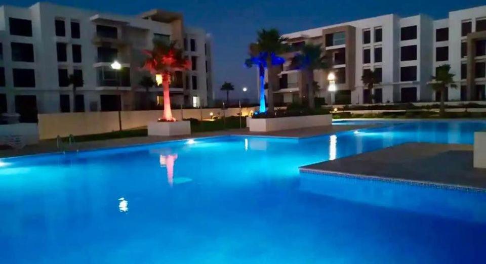 una gran piscina por la noche con edificios en Prestigia plage des nations F3 suite parentale, chambre 2 lits, salon séjour terrasse, 2 salle de bain, en Sidi Bouqnadel