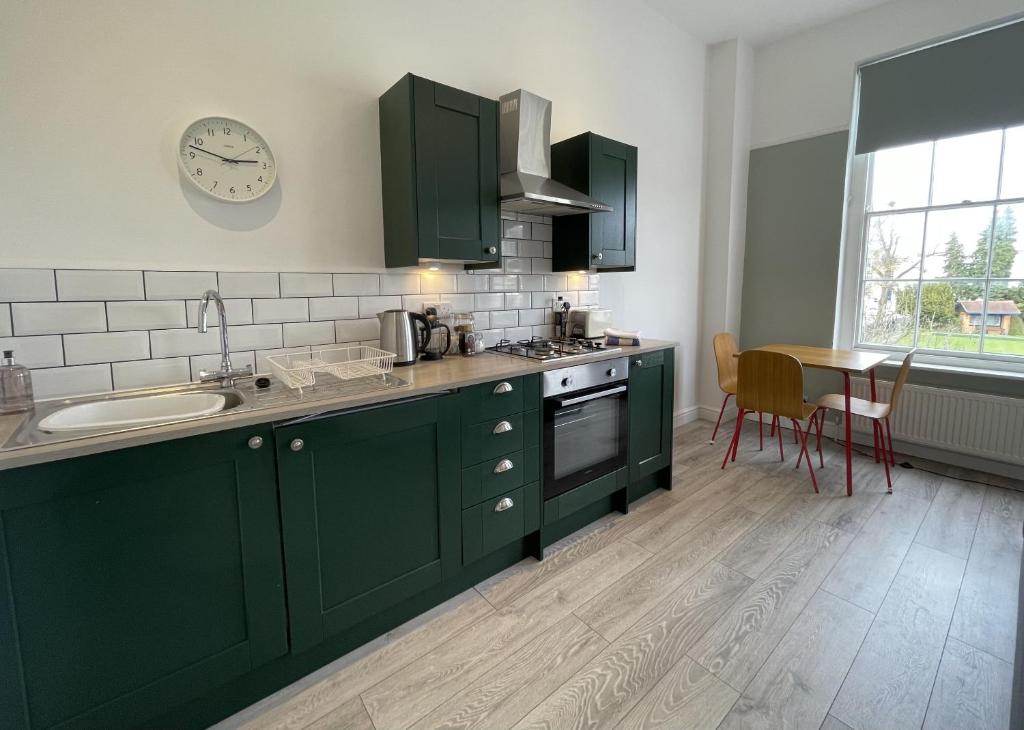 uma cozinha com armários verdes, um lavatório e uma mesa em Apartment 3 St Georges em Cheltenham