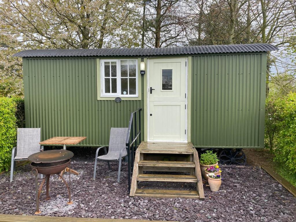 un cobertizo verde con escalera, mesa y sillas en Dawn Chorus Holidays, en Beccles