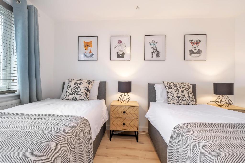 two beds in a bedroom with two lamps and pictures on the wall at MODERN Comfortable HOUSE in Peterborough