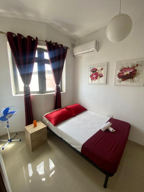 una camera da letto con un letto con lenzuola rosse e una finestra di Spiteri Court a San Pawl il-Baħar