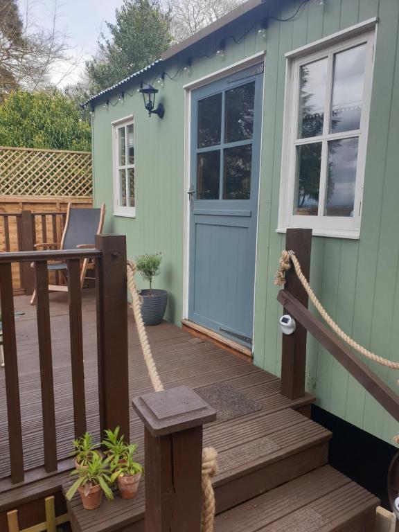 a green house with a wooden deck with a blue door at The Honeypot Shepherds Hut in Ross on Wye