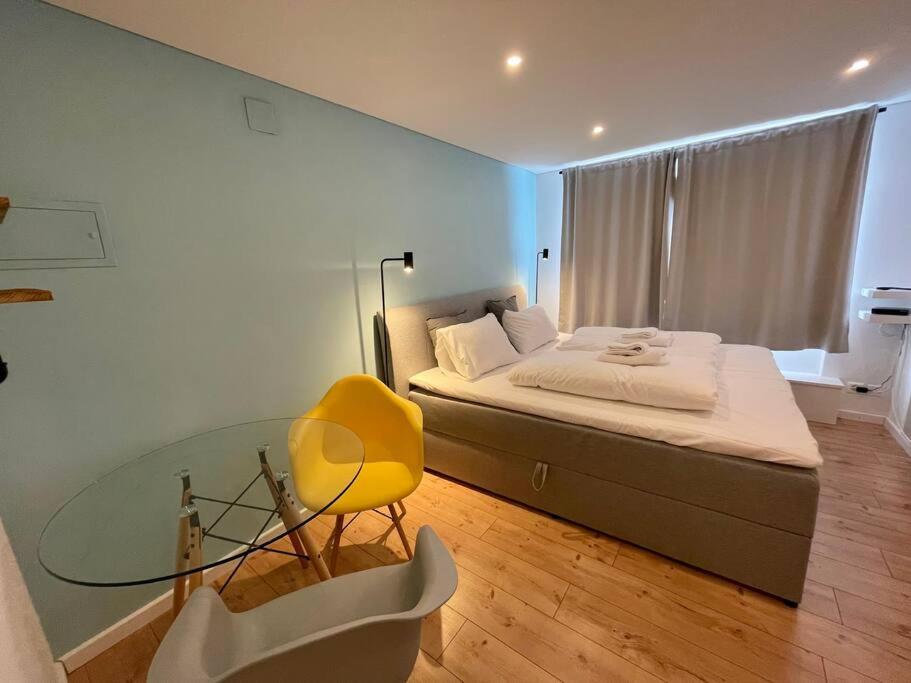 ein Schlafzimmer mit einem Glastisch, einem Bett und einem gelben Stuhl in der Unterkunft Studio Apt in FLIMS next to Caumasee in Flims