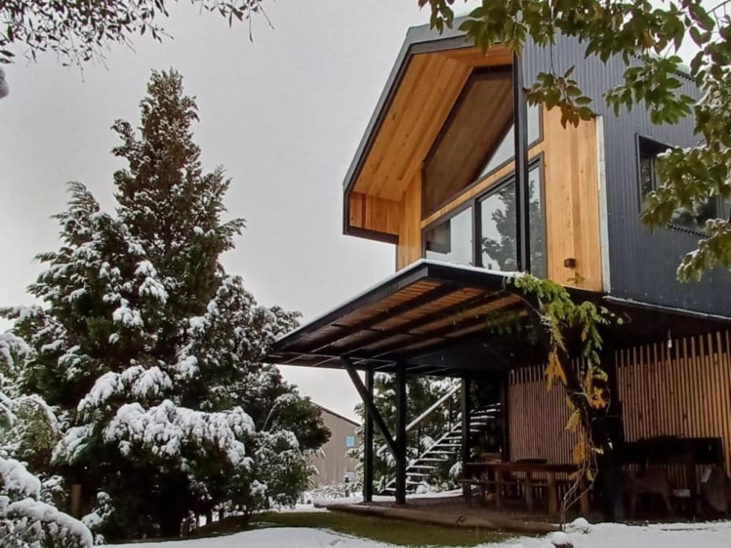une maison avec un toit en bois dans la neige dans l'établissement Casa de montaña La Cumba Patagonia., à San Martín de los Andes