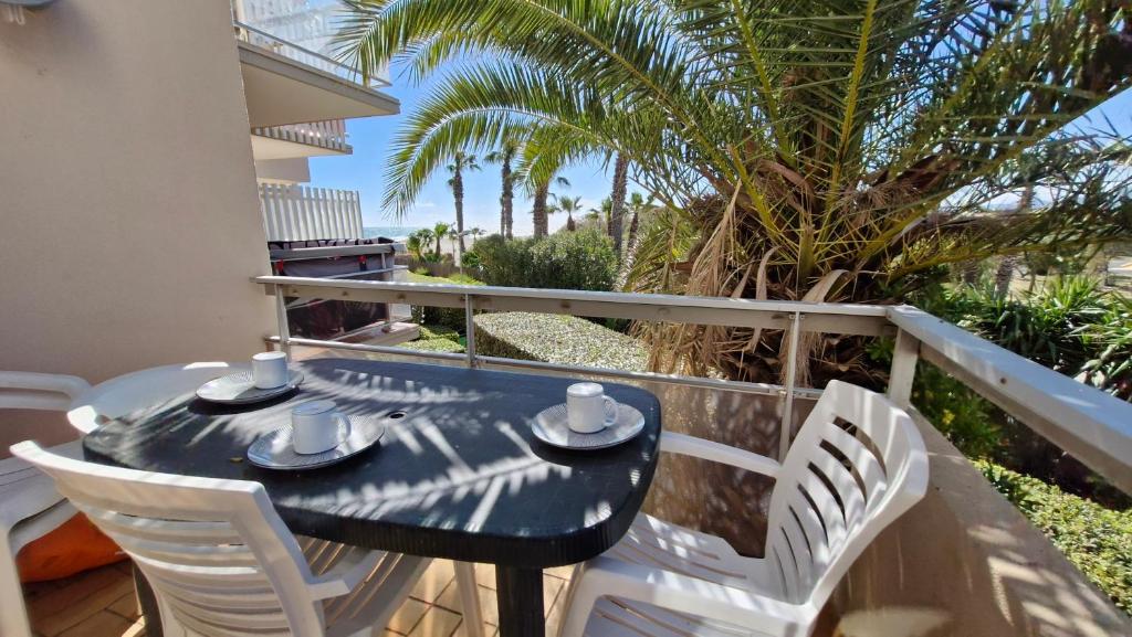 une table et des chaises noires sur un balcon avec des palmiers dans l'établissement Capitelles Appart accès direct plage et piscine - Balcon Parking - ref Tedal, à Saint-Cyprien
