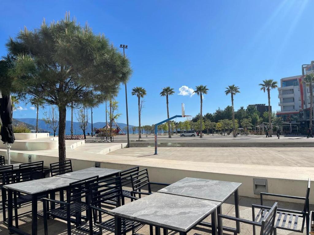 a patio with tables and chairs and a park with palm trees at FA_HOLIDAYS in Vlorë