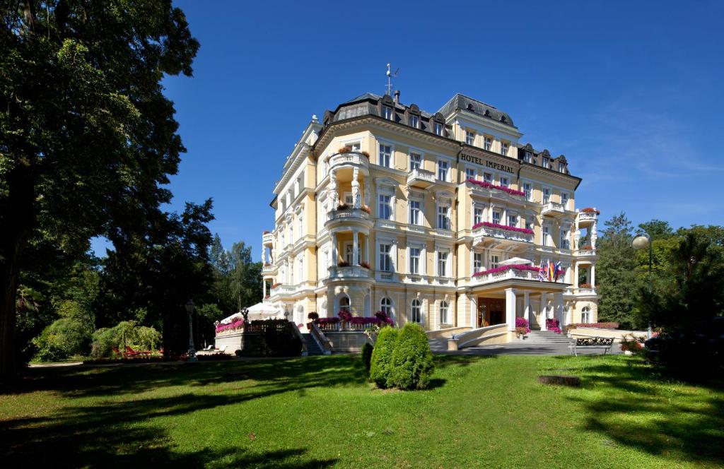 een groot wit gebouw bovenop een weelderig groen veld bij Imperial Spa & Kurhotel in Františkovy Lázně