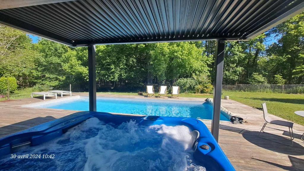 una bañera de hidromasaje azul bajo una cubierta junto a una piscina en Domaine de Cachaou Logis du Pujeau sauna & spa piscine chauffée, en Salles