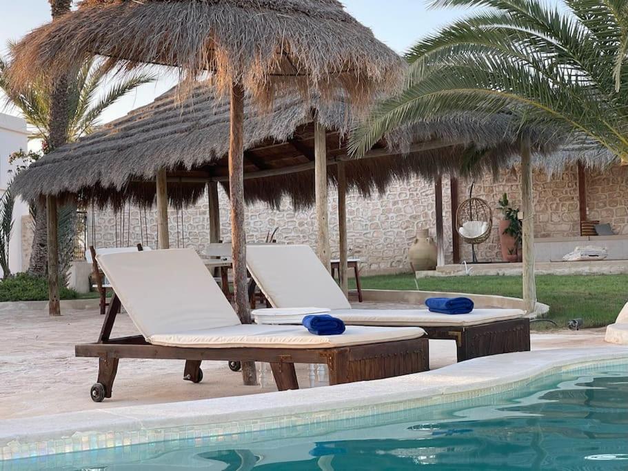 a pool with two lounge chairs and a thatch umbrella at Menzel Al karam, in Temlale