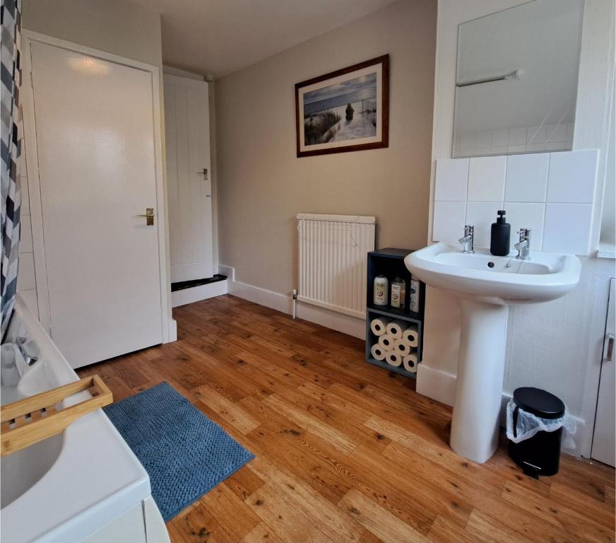 ein Badezimmer mit einem weißen Waschbecken und Holzböden in der Unterkunft Generous 3 bed in the heart of the village in Huntingdon