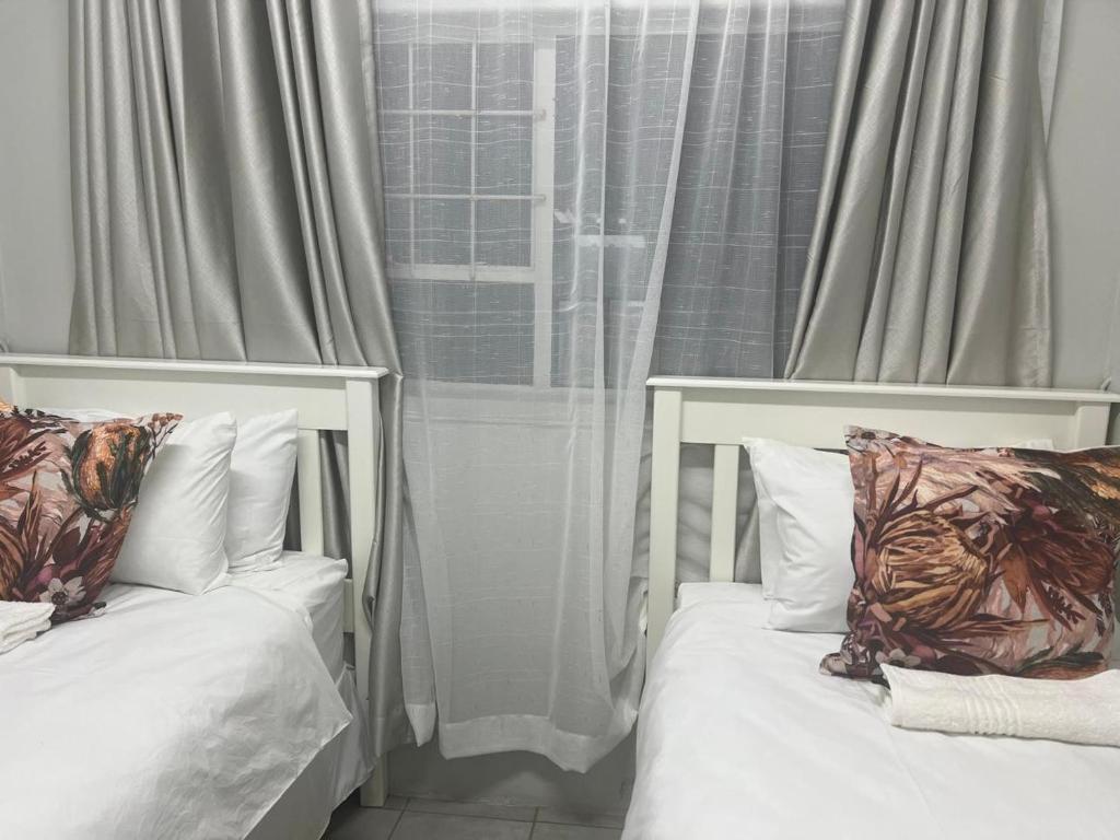 two beds with pillows in front of a window at The Space Guesthouse in Vryheid