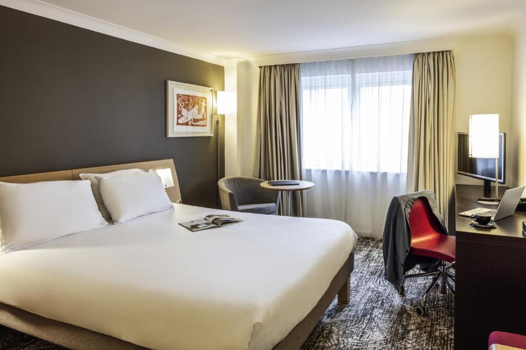 a hotel room with a bed and a desk and a window at Novotel Bristol Centre in Bristol