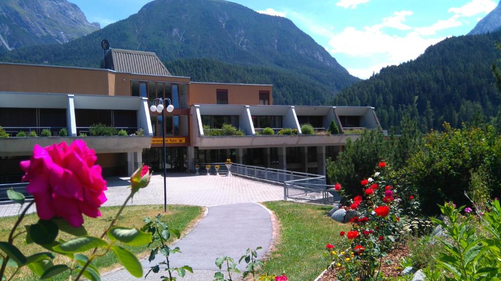 ein Gebäude mit Bergen im Hintergrund mit einer rosa Blume in der Unterkunft Tulai 104E in Scuol