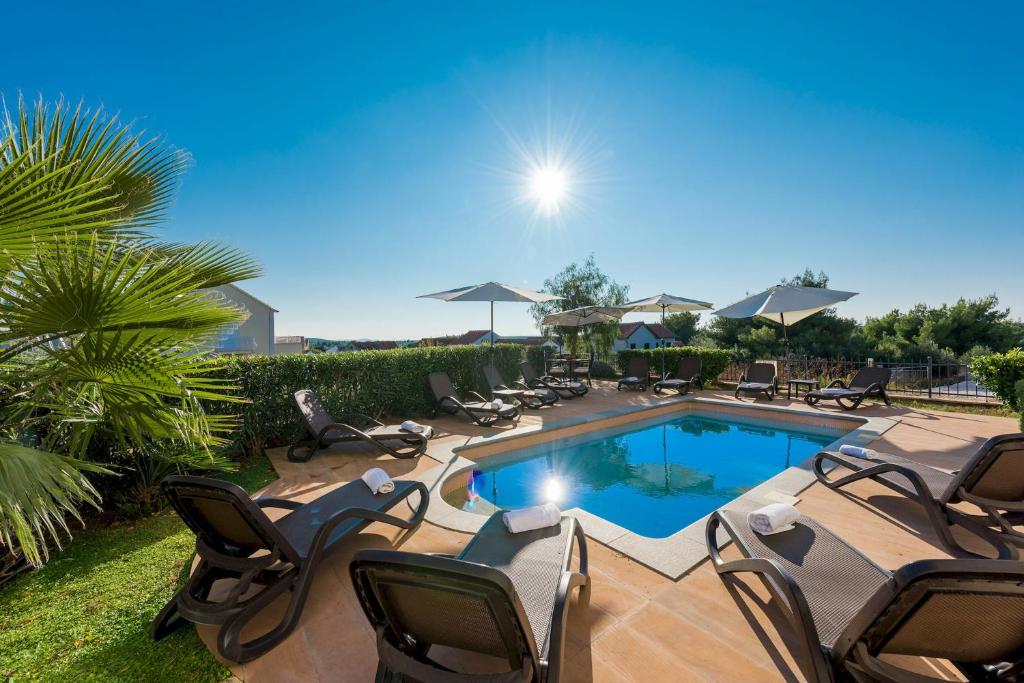 a swimming pool with chairs and umbrellas at Apartman Linda in Milna
