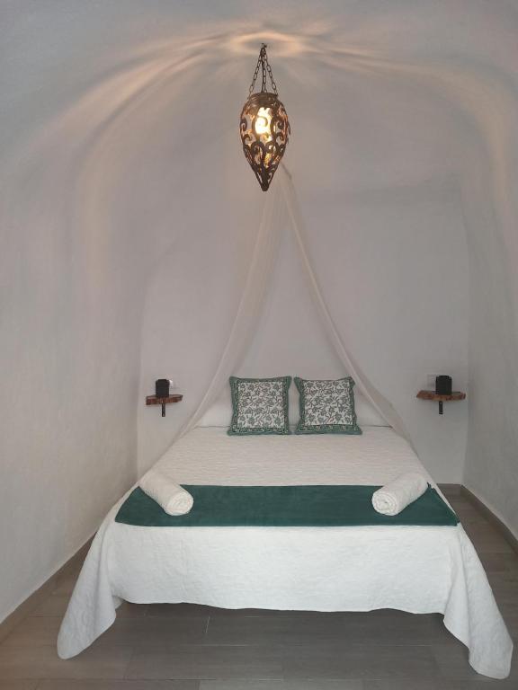 a bed in a white room with a chandelier at EL RINCON DEL ROMERAL in Pegalajar